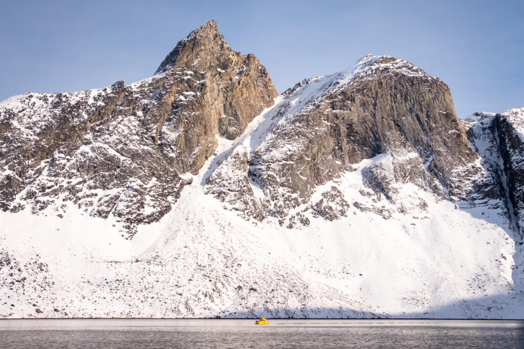 Yellow tour boat against a massive mountain backdrop in the Nuuk Fjord during winter - Greenland