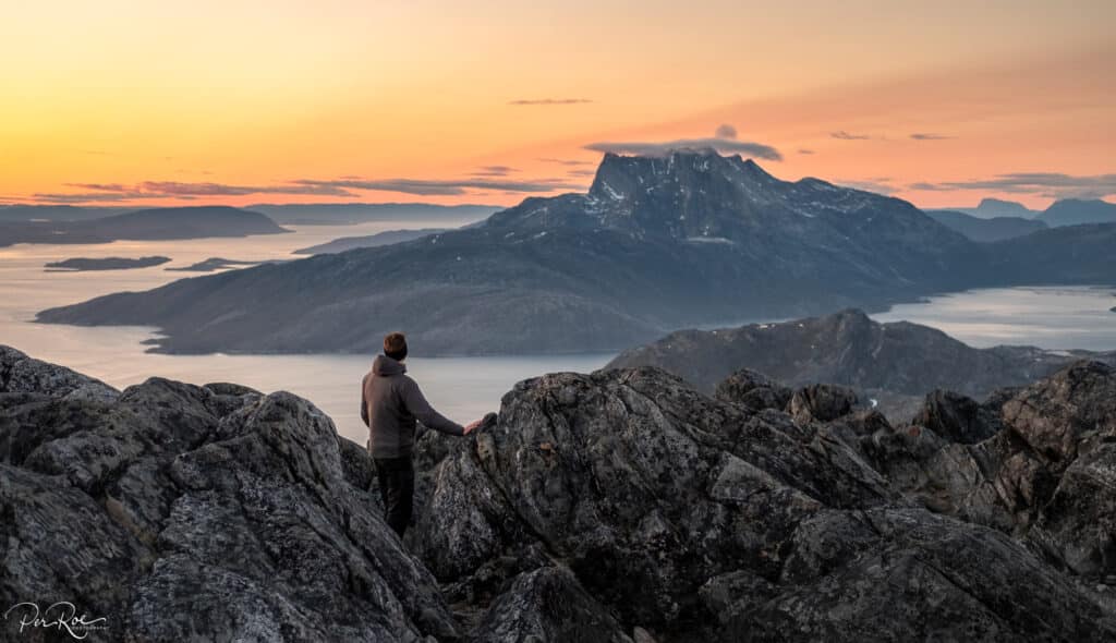 Person looking at the view of Sermitsiaq Mountain under an orange sunset sky - taken from the top of Store Malene near Nuuk