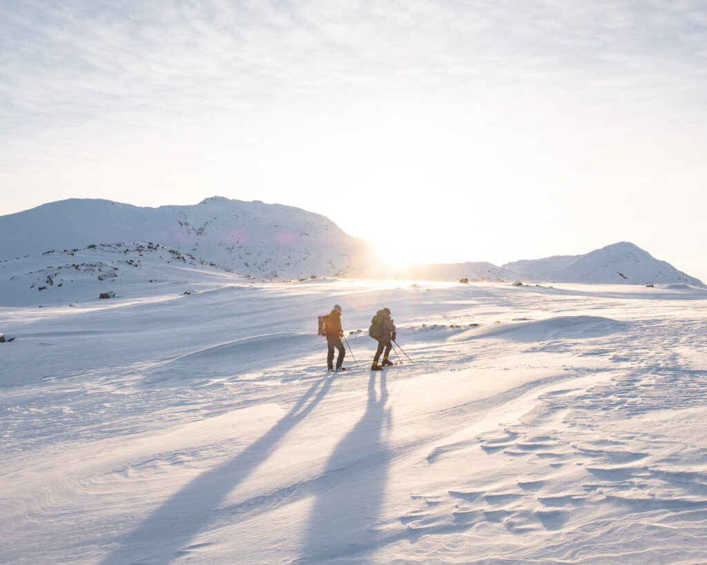 Two people snowshowing near Nuuk are backlit by the low sun - Greenland