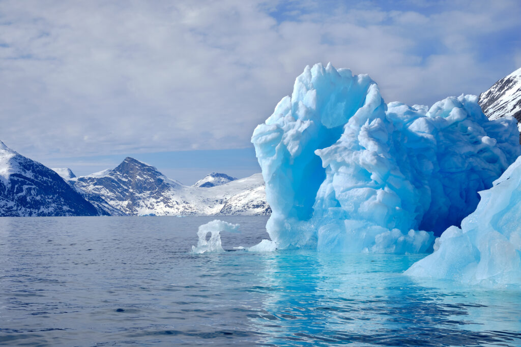 A large iceberg with mountains in the distance on a boat tour up the Nuuk Fjord with Guide to Greenland