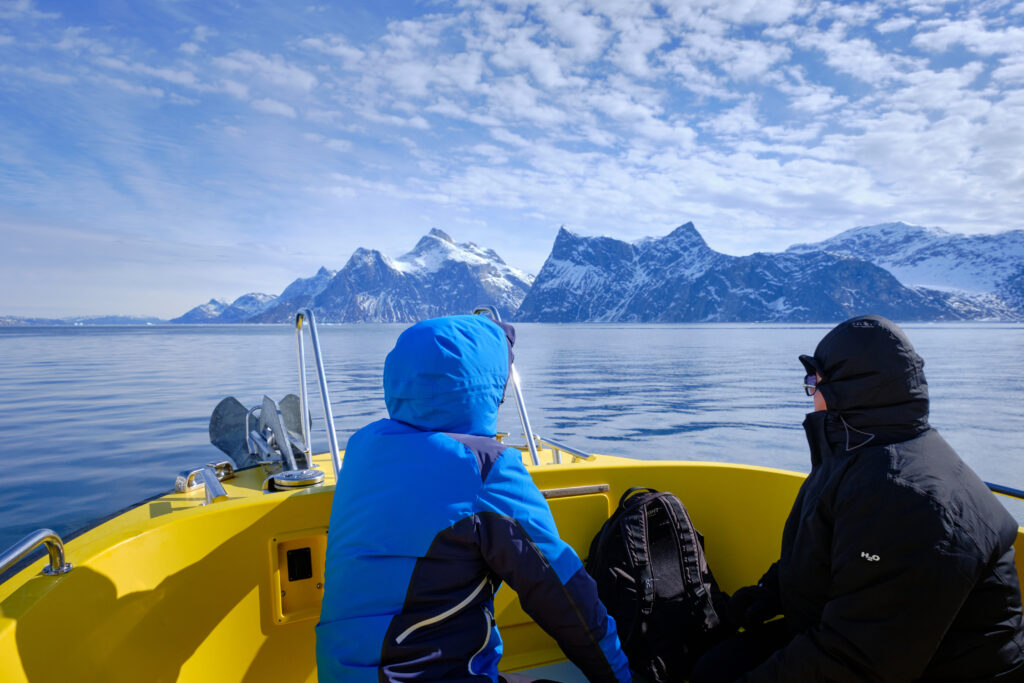 Two passengers sitting on the front deck admiring the mountains of the fjord on a boat tour to the Nuuk Icefjord with Guide to Greenland