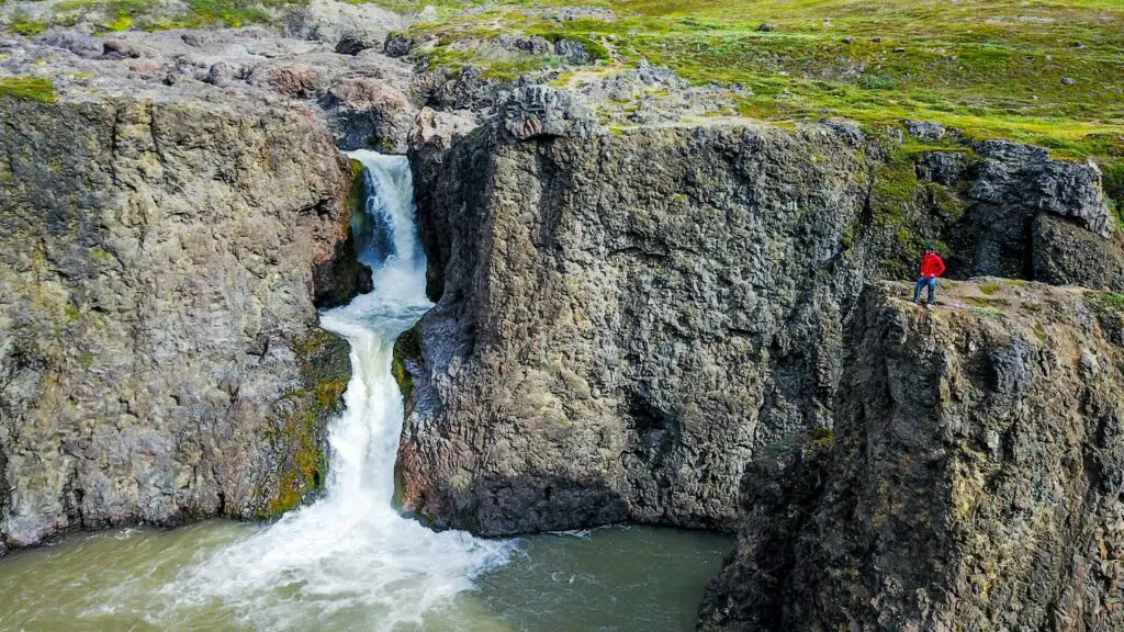 Man in red coat looking towards a waterfall at Disko Island in Greenland