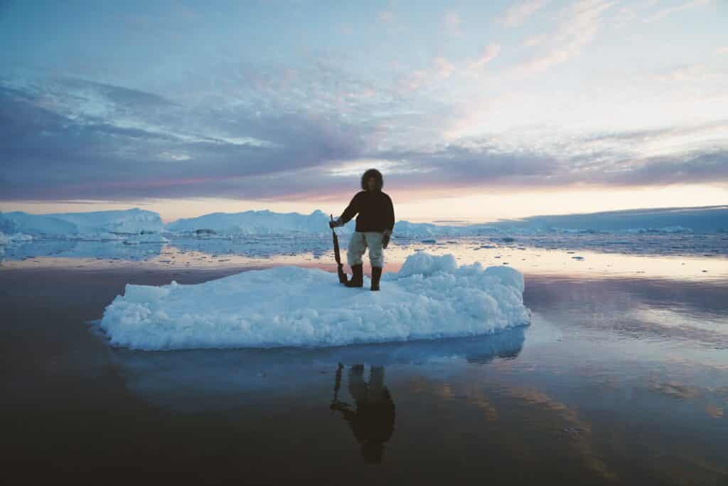 Man standing on a block of ice holding a riffle