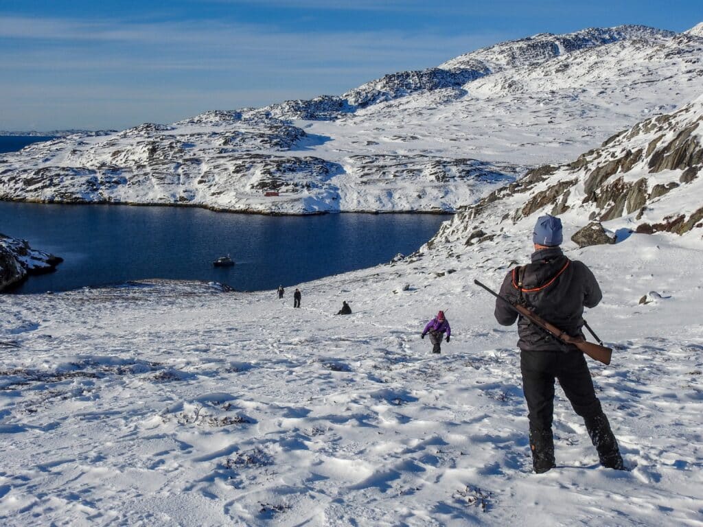 Man with riffle looking down to the fiord