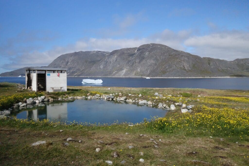 Small shelter next to a hot spring and an iceberg in the fjord