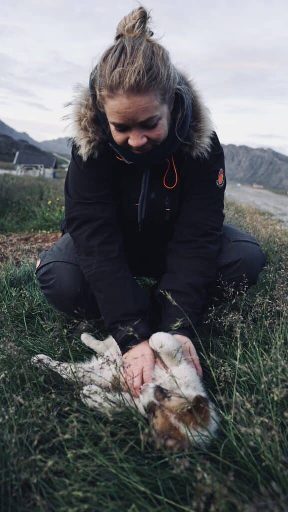 Frau spielt mit einem Schlittenhundwelpen im Gras