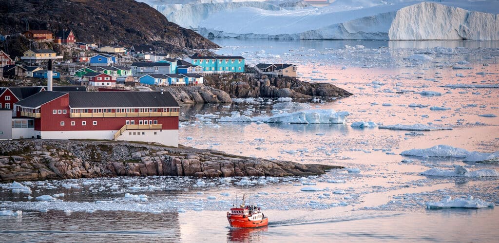 Boat coming into the harbour of Ilulissat with large icebergs and the town in the background