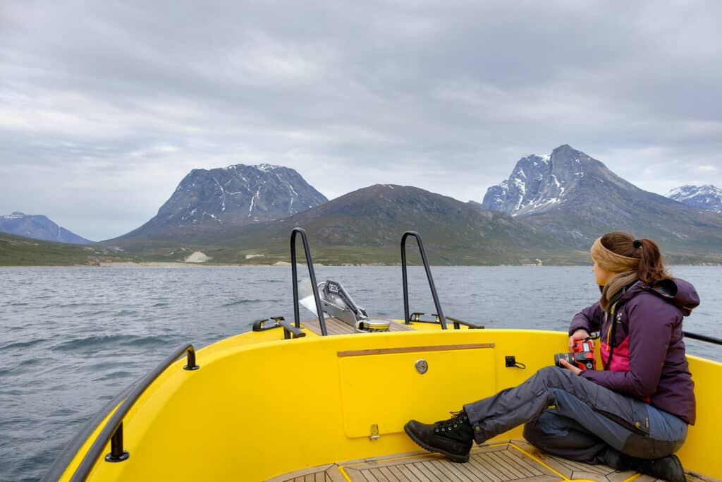 Person sitting in the front of a boat on a tour to Qooqqut with the settlement in the distance - summer - Guide to Greenland