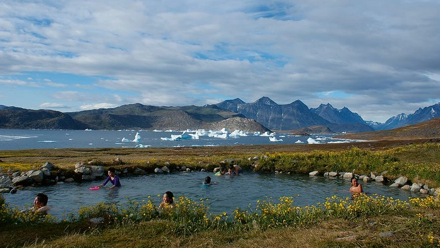 People bathing in hot spring with icebergs floating by in the fjord